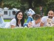 Happy family lying on grass with RV in the background, enjoying a sunny outdoor picnic.