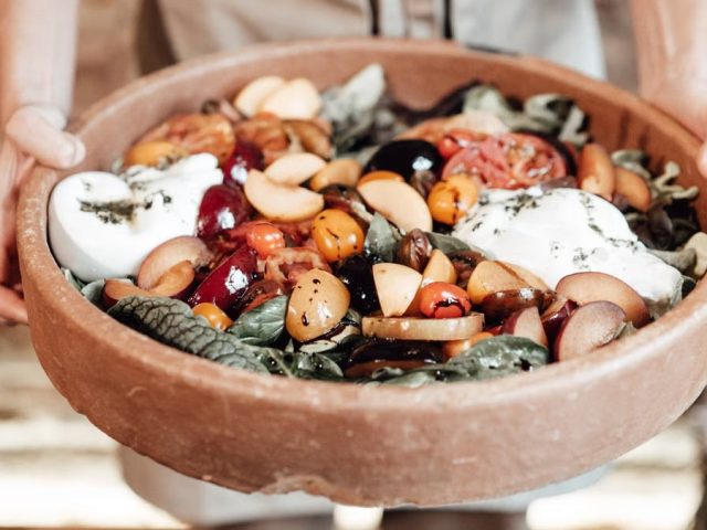 A vibrant rustic salad featuring fresh fruits, greens, and cheese in a wooden bowl, perfect for summer meals.